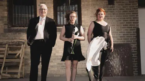 Student with clarinet and two adults standing in front of a building